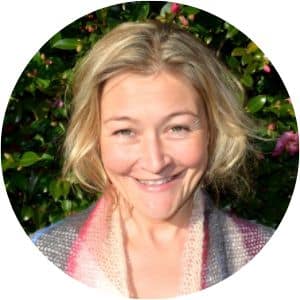 Anna Lloyd has short blonde wavy hair. She is wearing a colourful scarf and is looking at the camera, smiling.