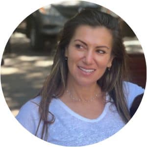 A woman, Nina Vucetic, is wearing a white shirt and is looking away from the camera, smiling. Her long brown hair is hanging down beside her shoulders.
